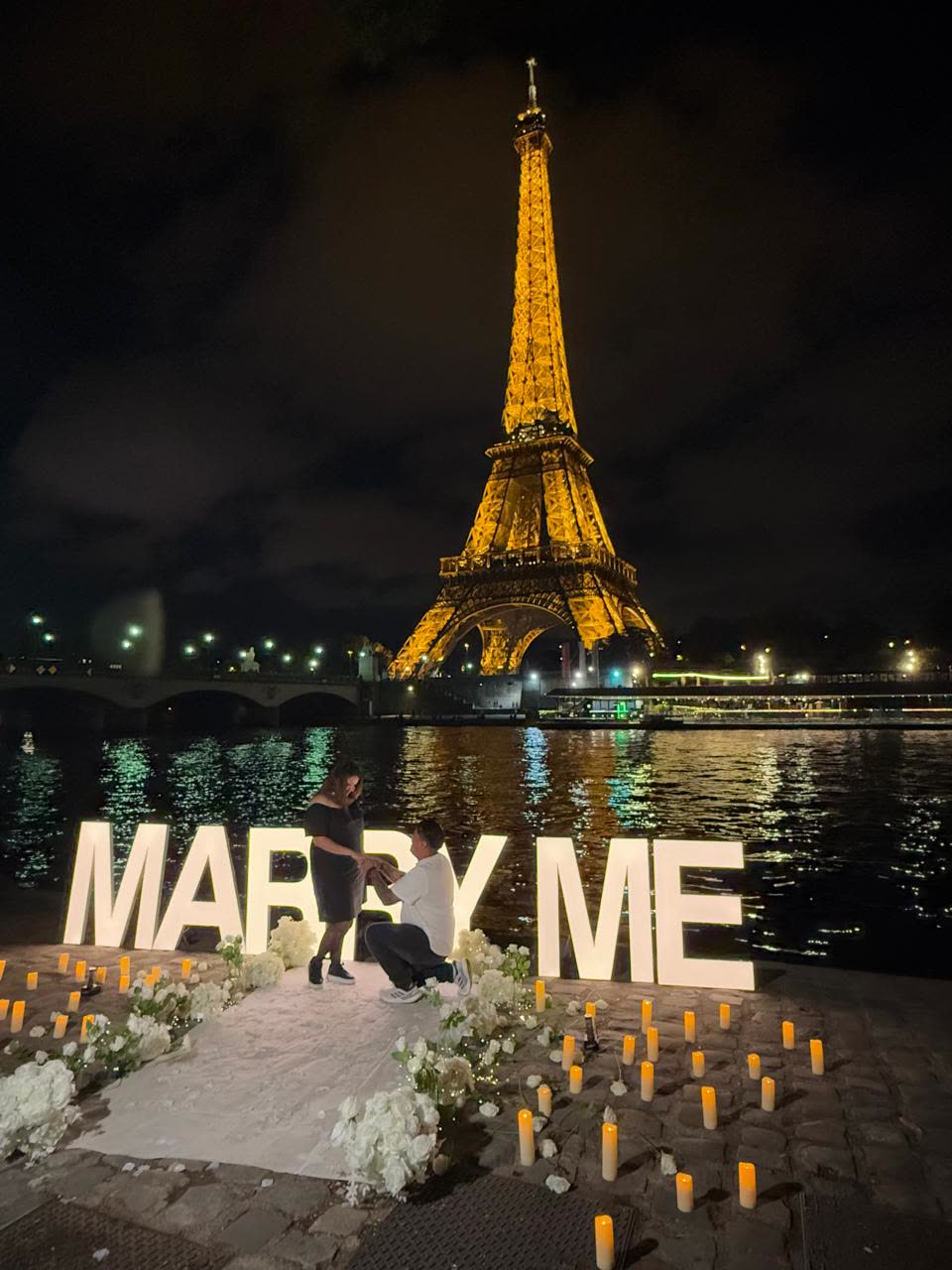 Álvaro arrodillado pidiéndole matrimonio a Tiffany junto al letrero Marry Me